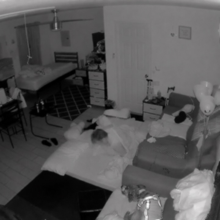 Lightly blurred benchmark scene showing an older adult reclined at floor level among bedding